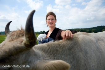 Bäuerin Anja hat ihren neugeborenen Sohn Leander im Tragetuch und steht bei ihren Kühen auf der Weide